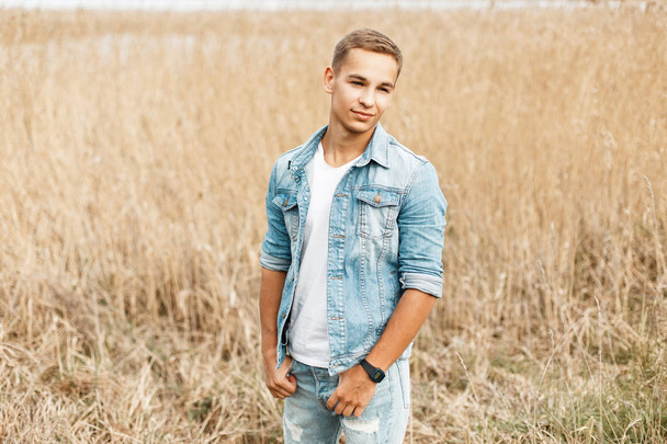 schöner junger Mann in stylischer Jeanskleidung draußen im Gras - Foto, Bild