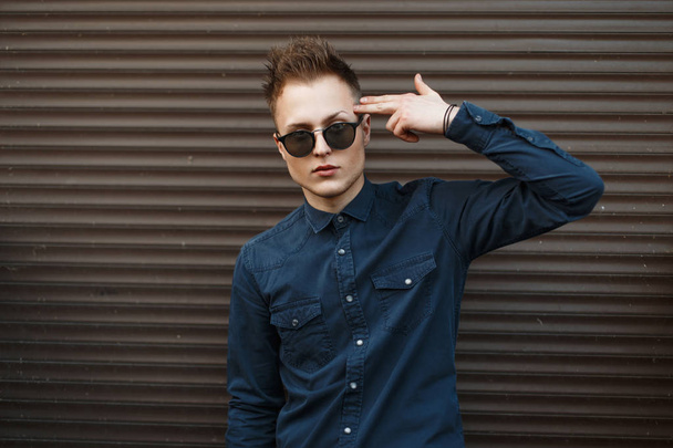 Handsome man in trendy sunglasses posing near metal wall - Photo, Image
