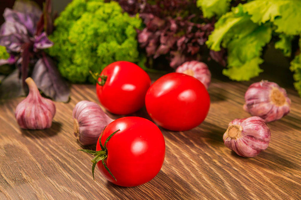 Fresh ripe tomatoes and garlic on a wooden table with a green salad in the background. Fresh vegetables. - Photo, Image