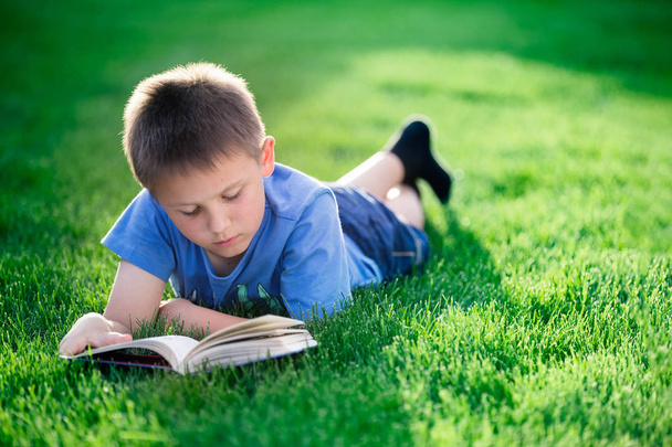 Boy reading book, lying down on green grass  - Фото, зображення