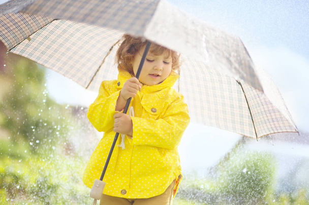 Cute toddler girl wearing yellow waterproof coat and boots with  - Foto, imagen