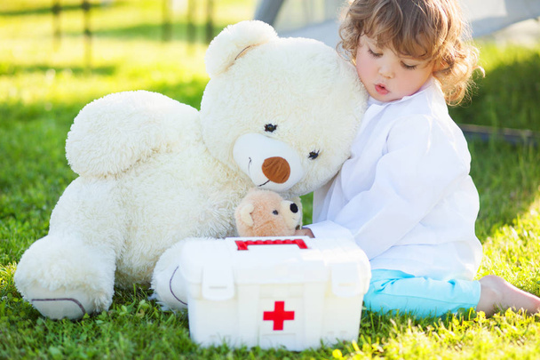 toddler girl playing doctor with plush toy bear outdoors - Foto, imagen