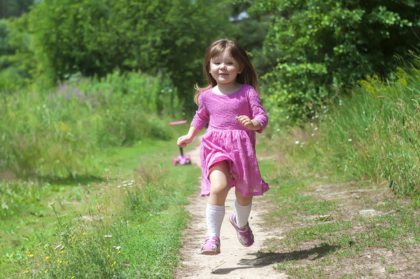 Adorable little girl in pink dress runs in the forest. Sunny day - Foto, afbeelding