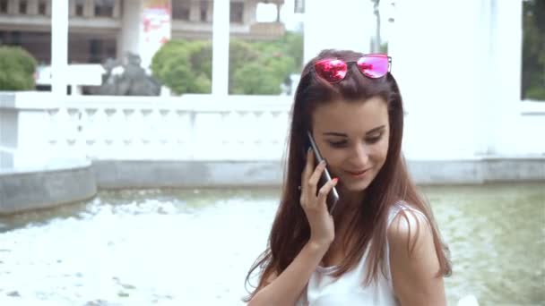 smiling girl talking on the phone near the fountain - Materiał filmowy, wideo
