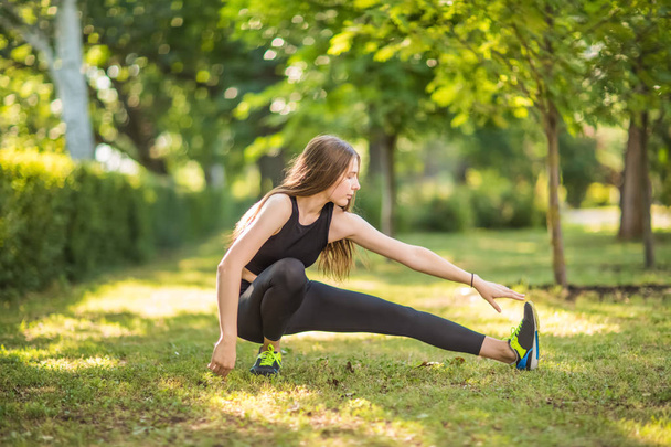 A girl with gorgeous and beautiful long light brown hair is doing sports exercises in the green grass. A girl looks athletic and happy. A sportswoman is doing exercise. - Fotografie, Obrázek