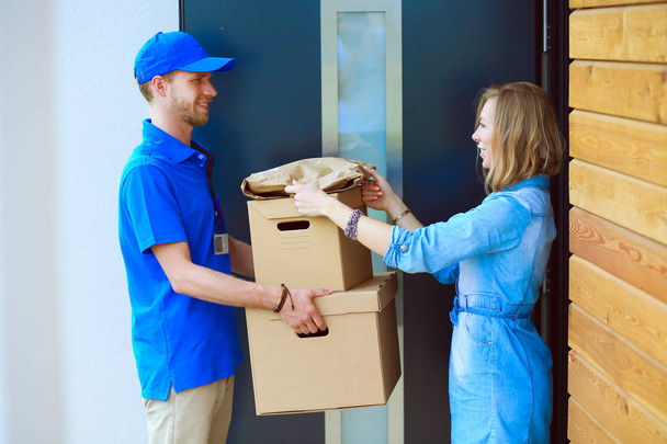 Smiling delivery man in blue uniform delivering parcel box to recipient - courier service concept - Foto, Imagen