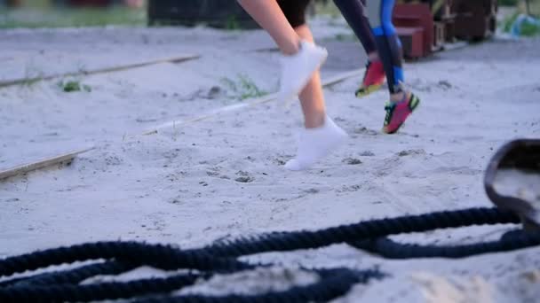 Mooie, slanke jonge vrouwen zijn bezig met fitness, springen, kracht oefeningen uit te voeren. Bij dageraad, in de buurt van een lading kraan, op het strand zand steengroeve, - Video