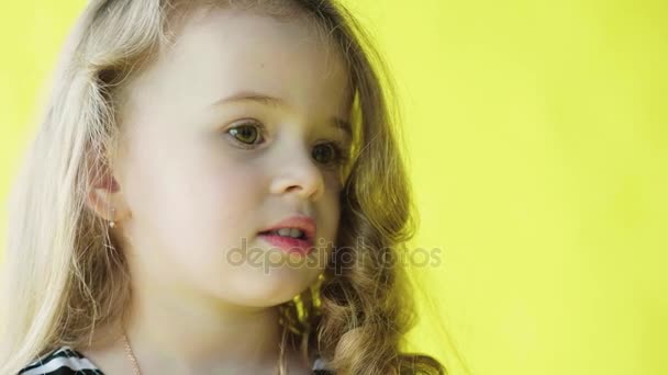 Linda niña sonriente con el pelo rizado. Retrato de primer plano sobre fondo amarillo. Movimiento lento
 - Imágenes, Vídeo
