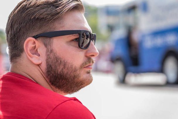 handsome young man sitting outside in summer with sunglasses and beard - Fotografie, Obrázek