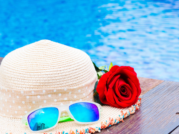 Flores rosas rojas con sombrero de verano y gafas de sol junto a la piscina. Vacaciones y relajación, concepto de viaje de verano
. - Foto, Imagen