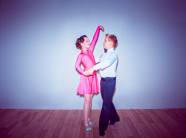 der kleine Junge und das Mädchen posieren im Tanzstudio auf blauem Grund in Tangopose. das Konzept des Standardtanzes - Foto, Bild