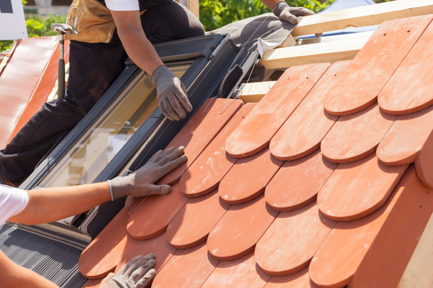Manos de tejado colocando baldosas en el techo. Instalación de baldosas rojas naturales. Techo con ventanas de mansarda
 - Foto, imagen