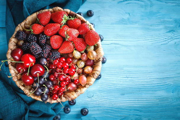 Ripe berries in a wicker plate on a blue wooden table. - 写真・画像