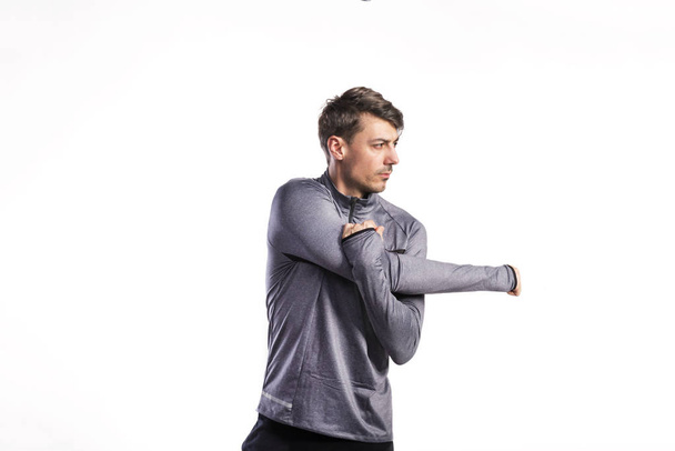 Fit man in gray sweatshirt stretching arms, studio shot. - Foto, Bild