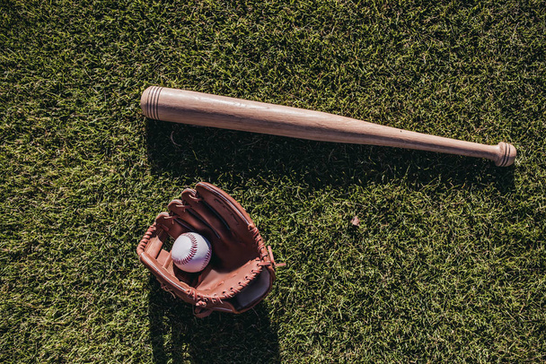 Bate de béisbol, pelota y guante está acostado sobre hierba verde
 - Foto, imagen