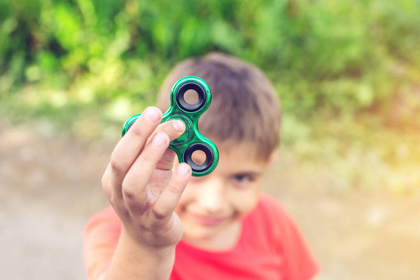 Een jongen speelt met spinner draaien het in zijn hand op buitenshuis. Trends in kinderspeelgoed Antistress - Foto, afbeelding