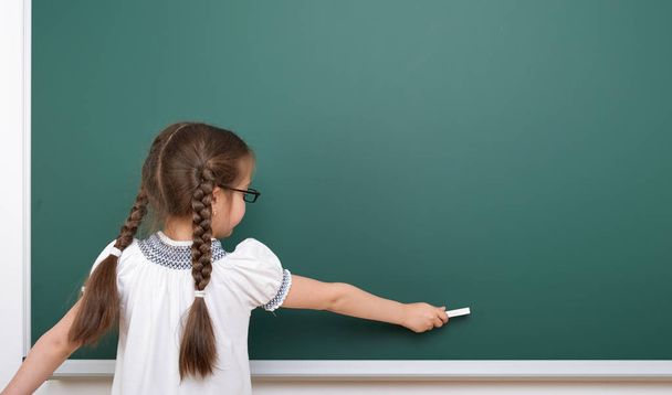 Schoolgirl writing chalk on a blackboard, empty space, education concept - Фото, изображение