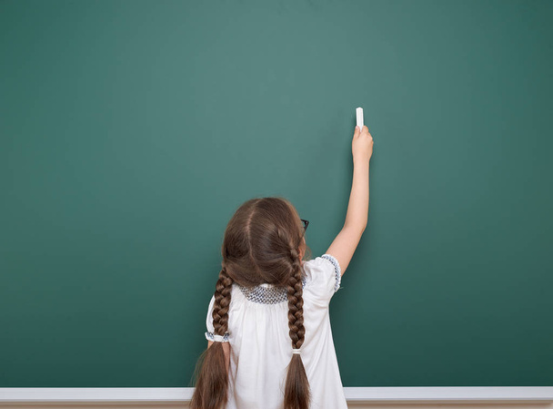 Schoolgirl writing chalk on a blackboard, empty space, education concept - Фото, изображение