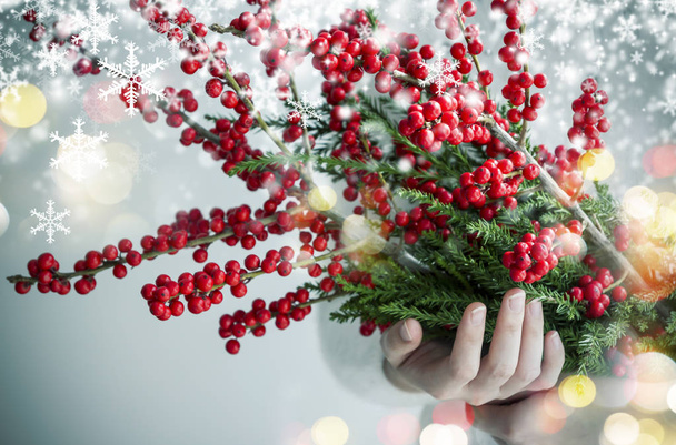 Christmas and new year concept design of woman hands holding ilex verticillata or winterberry with snow and light bokeh - Photo, Image