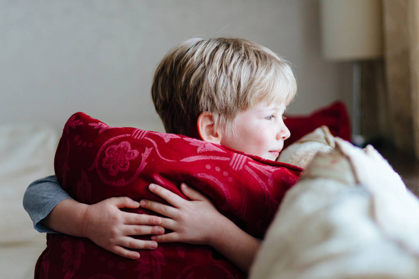 Primo piano di bel bambino che abbraccia un cuscino rosso e distoglie lo sguardo
. - Foto, immagini