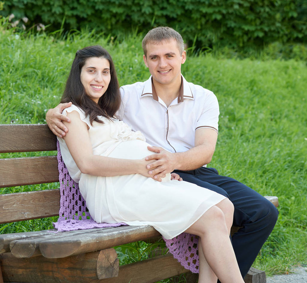 ευτυχισμένο ζευγάρι στο πάρκο της πόλης το καλοκαίρι υπαίθρια, έγκυος γυναίκα, λαμπρό ηλιόλουστη μέρα και πράσινο γρασίδι, όμορφη άνθρωποι πορτρέτο - Φωτογραφία, εικόνα