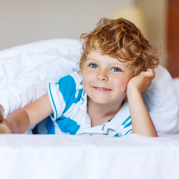 Adorable kid boy after sleeping in his white bed with toy - Photo, Image