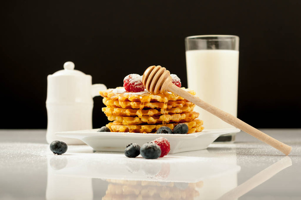 Belgian waffles with raspberries and sieving sugar powder and honey served with jug of milk on a white table - Photo, Image