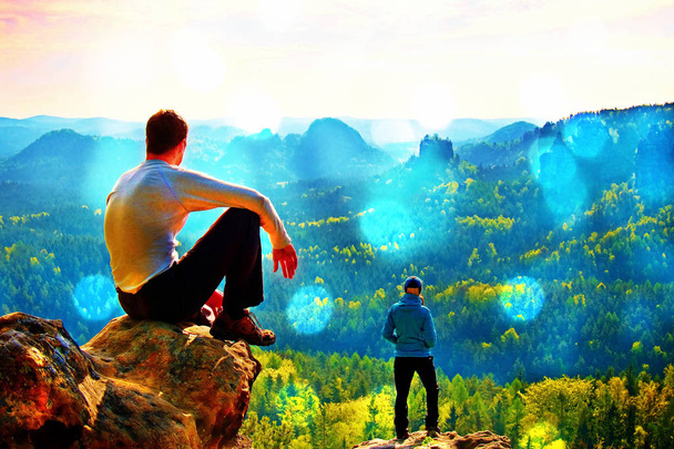 Filmkorrel. Jongen en meisje toeristen verblijven op klif en denken. Dromerige fogy landschap, blauwe mistige zonsopgang in een prachtige vallei hieronder - Foto, afbeelding