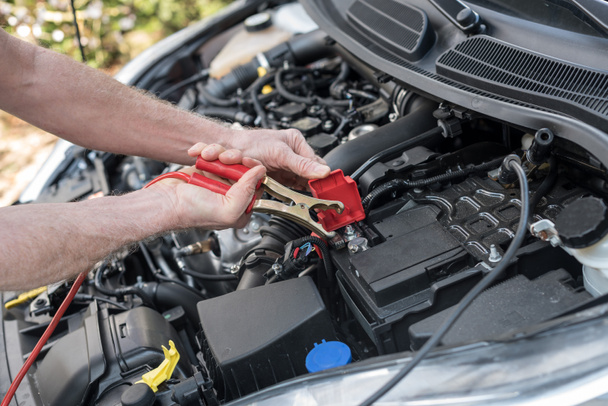 Autó akkumulátor jumper kábel segítségével autószerelő kezében - Fotó, kép
