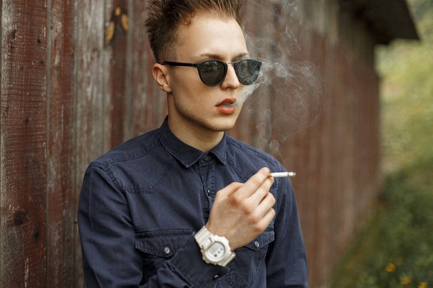 Κομψό όμορφος άντρας καπνίζει ένα τσιγάρο κοντά σε ένα τοίχο vintage - Φωτογραφία, εικόνα