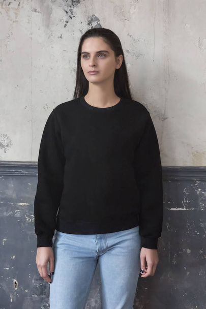 Jonge hipster meisje dragen van lege zwarte katoenen sweatshirt met kopie ruimte voor uw ontwerp of logo, mock-up van paarse sjabloon womens hoodie, grijs muur op de achtergrond - Foto, afbeelding