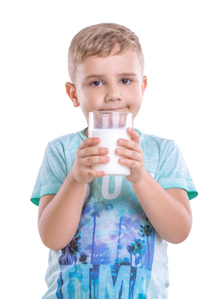 Smiling handsome boy holding a glass of milk in his hands isolated on a white background. The boy is wearing a blue T-shirt and is standing with a drain of fresh milk. - Photo, Image