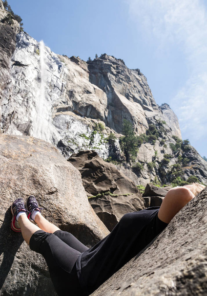 Uma jovem aventureira em roupas atléticas repousa sobre uma pedra abaixo de Bridalveil Falls, no Parque Nacional de Yosemite
. - Foto, Imagem