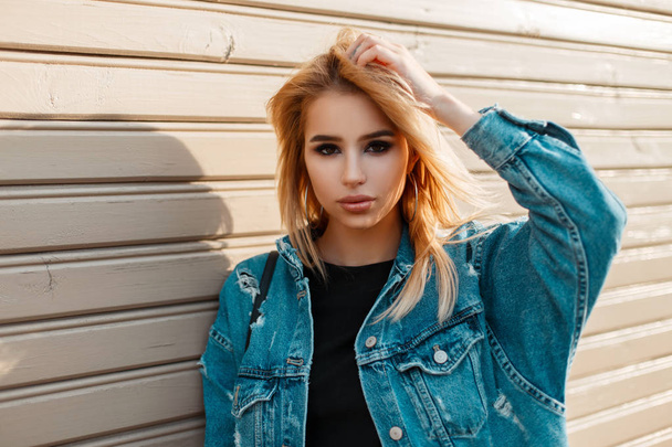 Beautiful young blond model woman in vintage jeans clothes near a wooden wall with timber - Photo, Image