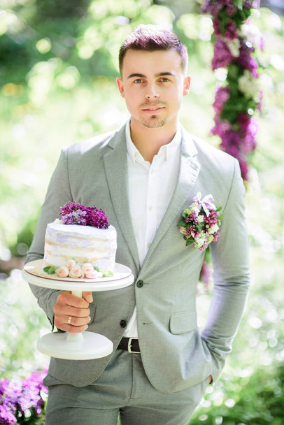 Groom poses with little rustic wedding cake  - Photo, image