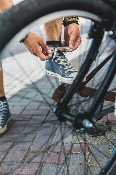 Young man tying his shoelaces before starting daily bike trips, closeup. Lifestyle Activity Footwear Concept - Fotó, kép