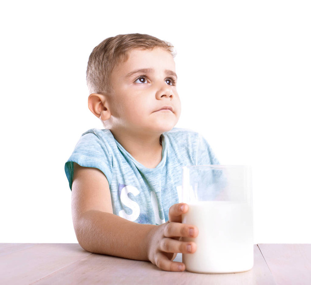 A cute and nice little boy in a blue T-shirt holds a glass of a fresh and organic milkshake and looks away, isolated on a white background. - Foto, Bild