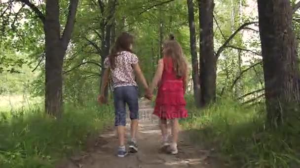 two little girls hold hands and walk down the green alley. children walk outdoors. two little sisters - Footage, Video