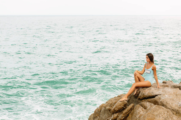 Beautiful girl in blue swimsuit sit on big stone. - Photo, Image