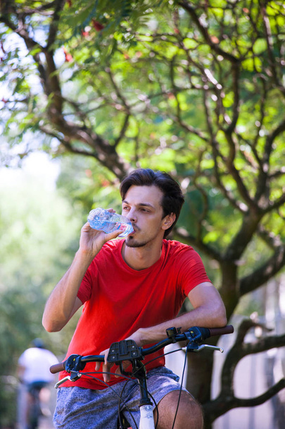 jeune homme assis sur le vélo dans le bois au repos boire de l'eau
  - Photo, image