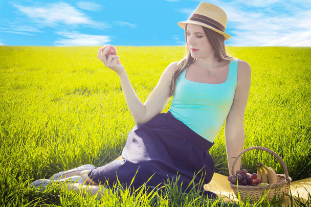 Chica con una manzana contra el cielo y la hierba
 - Foto, imagen