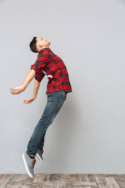 Concentrated young man jumping over grey wall. - Фото, зображення