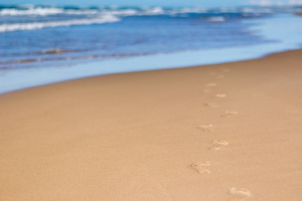 Jalanjälkiä hiekassa rannalla johtaa kohti merta
 - Valokuva, kuva