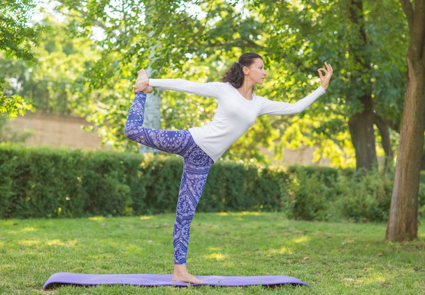 Beautiful girl doing asanas on a natural background. A sports girl stretching on a purple mat. Healthy fitness lifestyle.  - Photo, image