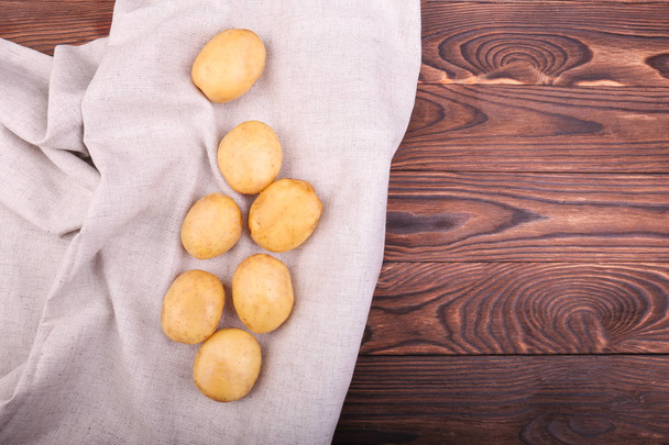 A close-up of some raw, fresh and new potatoes are scattered on a grey fabric on a dark brown wooden table, top view. Fresh vegetables.  - Foto, Bild