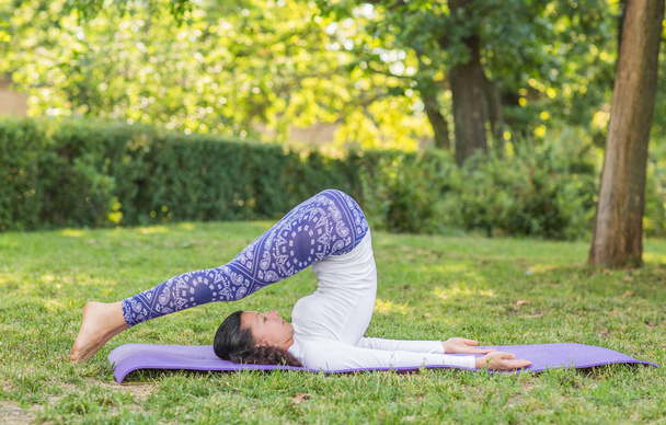 An attractive girl exercising in a park. Training in the morning. Young woman practicing different asanas.  - Photo, Image