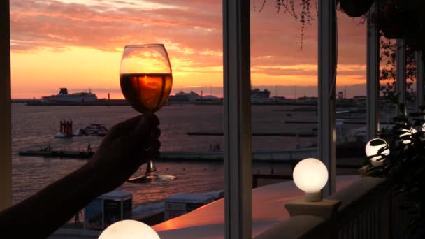 A man is holding a glass of alcohol against the sunset over the sea. close-up. Slow motion - Záběry, video