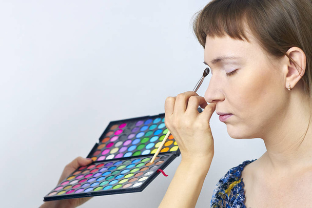 Female makeup model and visagiste hand with eyeshadow brush and pallette - on the right side - Photo, Image