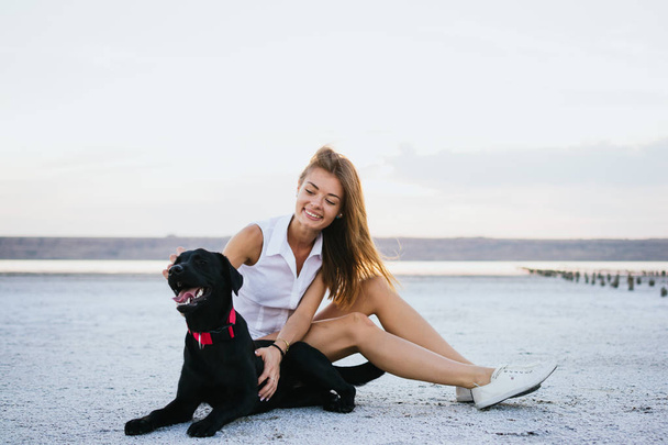 若い女性の夕暮れビーチにラブラドル ・ レトリーバー犬犬とハグ - 写真・画像