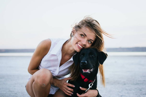 Happy young female with labrador retriever dog on the beach at sunset - Photo, image
